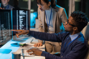 A man and a woman sitting at a desk looking at code on a computer